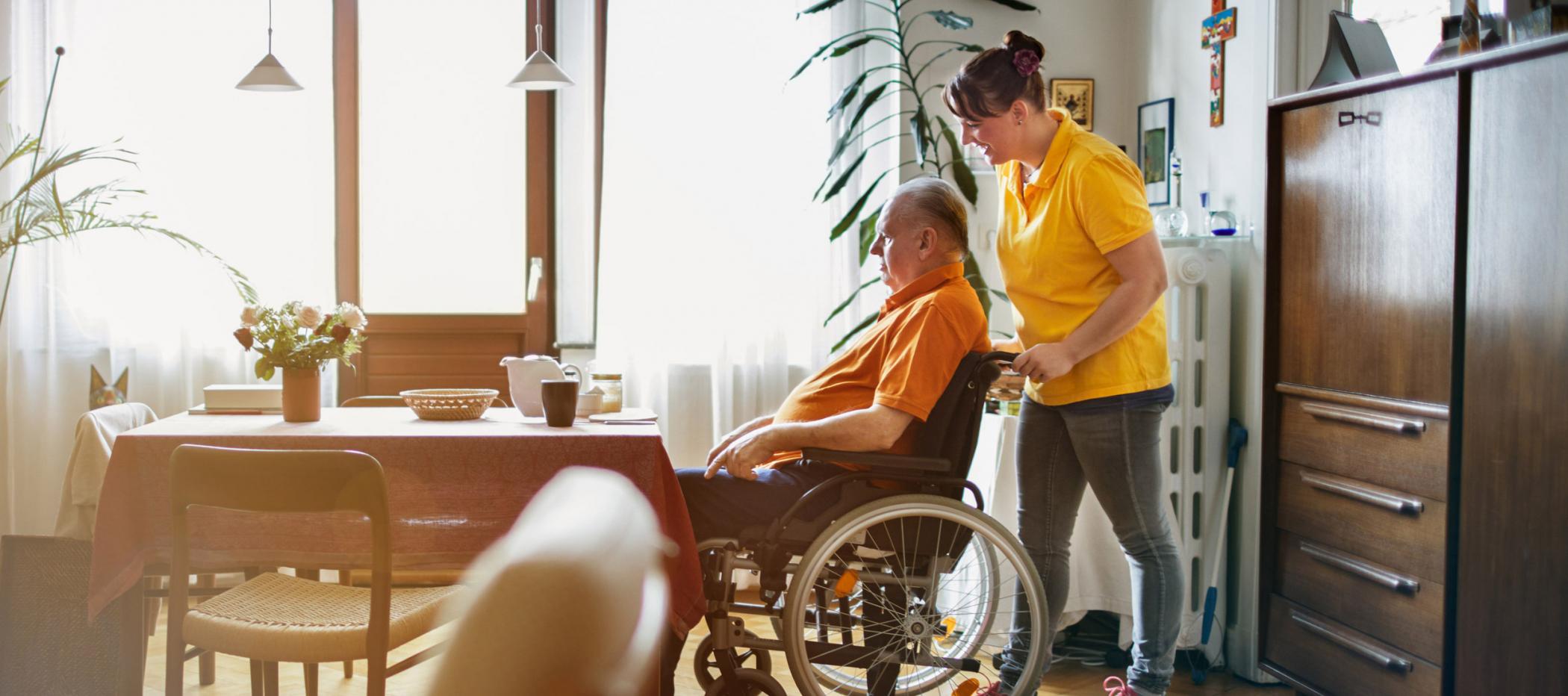 Pflegefachkraft schiebt Kunden im Rollstuhl.